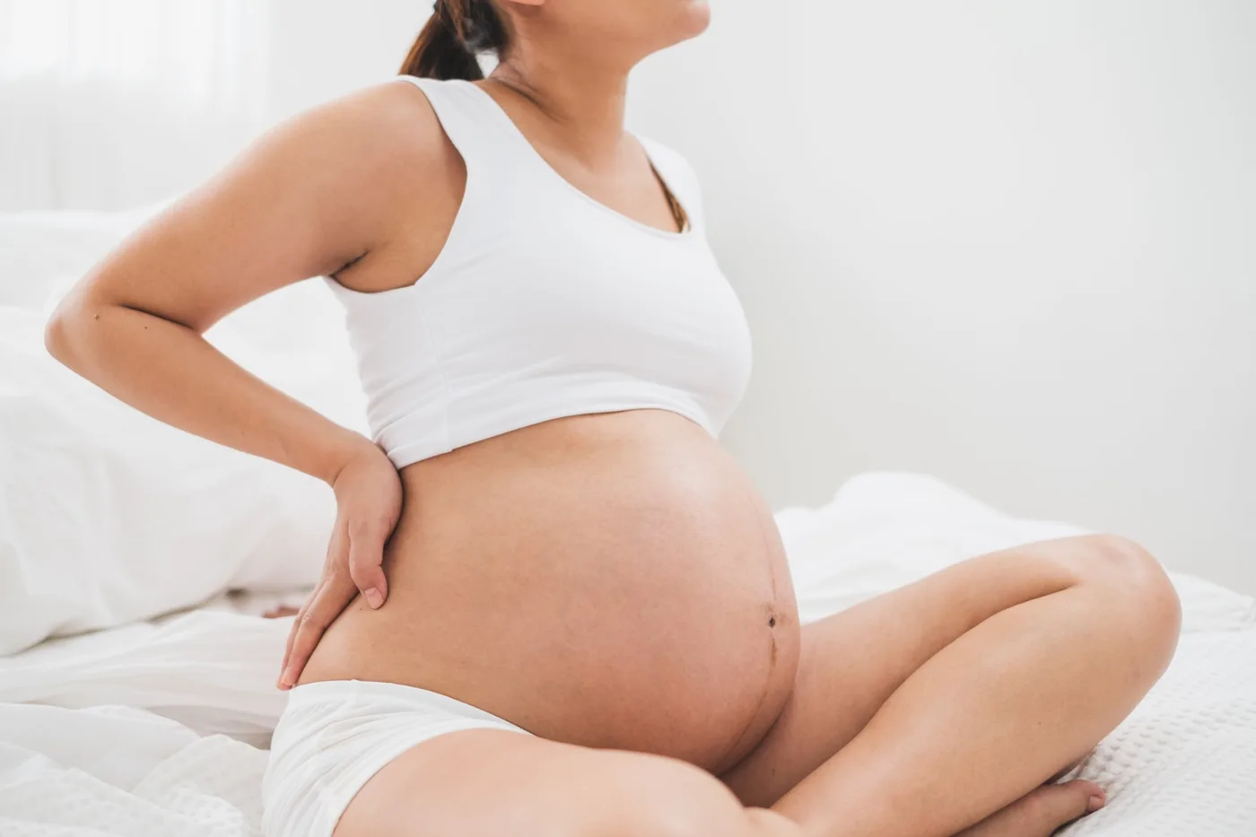 Gravid kvinne som sitter i senga og holder seg på korsryggen