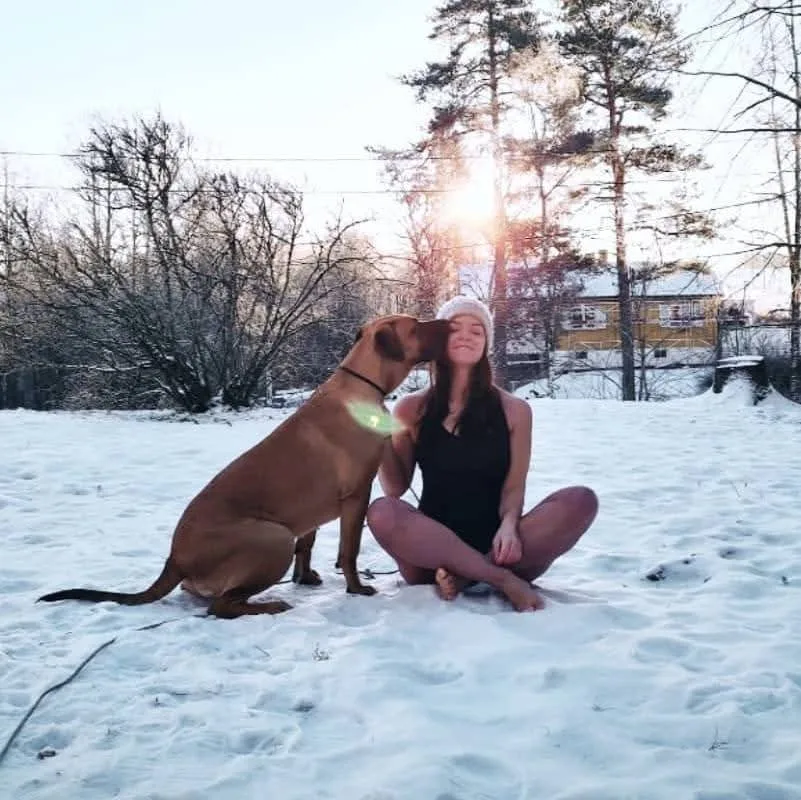 Sara Nordanger i badedrakt og lue i snøen, sammen med hunden Salsa